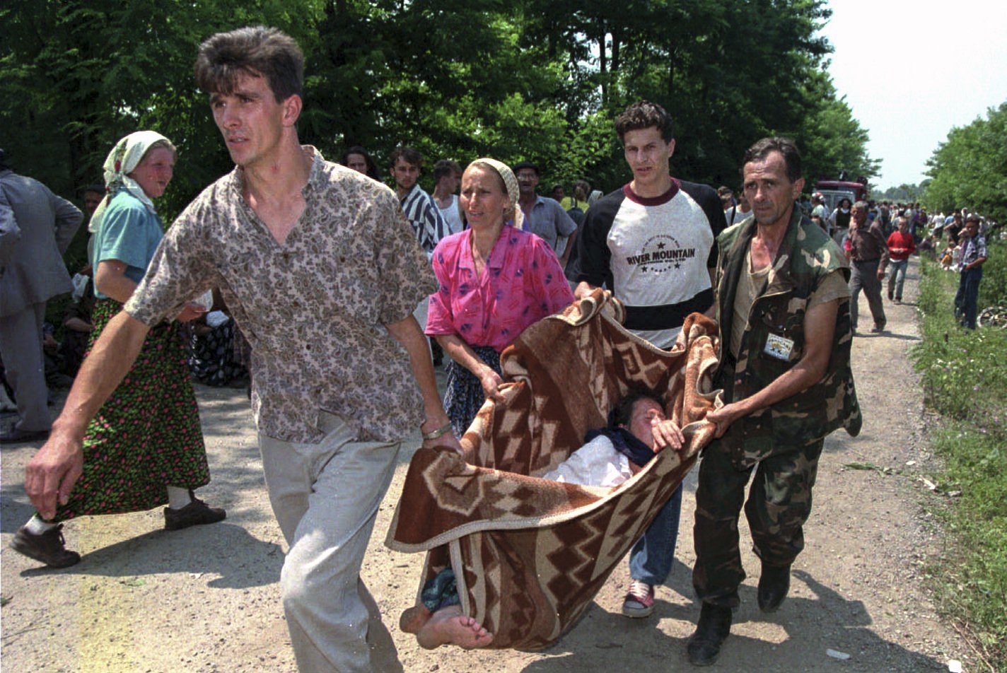 FILE- In this Thursday, July 13, 1995, file picture, refugees and a Bosnian government soldier carry a sick woman on a makeshift stretcher to a hospital inside a U.N. base outside Tuzla.  Survivors of the genocide in the eastern Bosnian town of Srebrenica, mainly women, will on Saturday July 11, 2020, commemorate the 25th anniversary of the slaughter of their fathers and brothers, husbands and sons. (AP Photo/Darko Bandic, File)