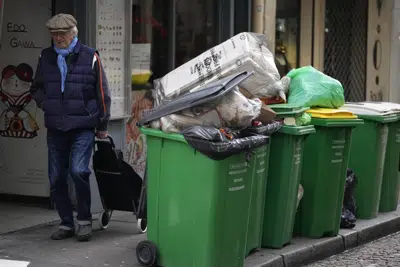 Un hombre camina frente a botes de basura sin recolectar, el jueves 9 de marzo de 2023, en París. (AP Foto/Michel Euler)