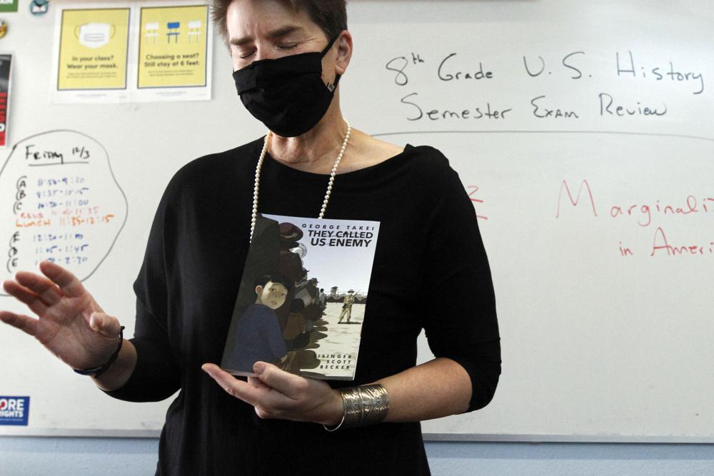 FILE - History teacher Wendy Leighton holds a copy of "They Called us Enemy," about the internment of Japanese Americans, while speaking about being marginalized with her students at Monte del Sol Charter School on Dec. 3, 2021, in Santa Fe, N.M. As conservative-run states across the U.S. move to restrict discussion of race, gender, and identity in the classroom, progressive-run states are trying to prioritize those discussions. In New Mexico, education officials are moving forward with a social studies curriculum that increases focus on identity, race and "privilege or systemic inequity." (AP Photo/Cedar Attanasio, File)