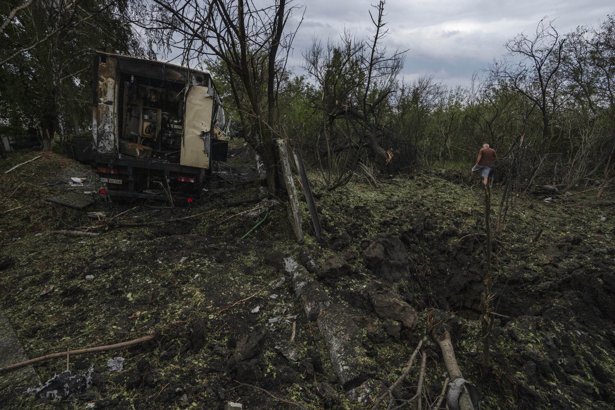 A man walks away from a crater in the aftermath of a Russian rocket attack, that killed 35-year-old Anna Protsenko, on the outskirts of Pokrovsk, eastern Ukraine, Saturday, July 16, 2022. Protsenko was killed two days after coming home. She had done what authorities wanted, evacuating eastern Ukraine's Donetsk region as Russian forces move closer, but starting a new life elsewhere was uncomfortable and expensive. (AP Photo/Nariman El-Mofty)