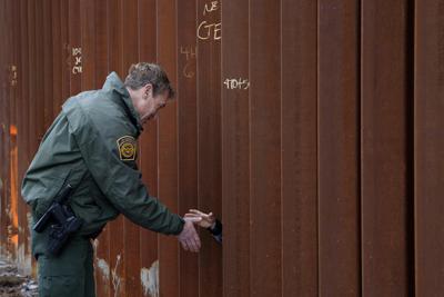 Esta fotografía del 15 de enero de 2019 muestra a Rodney Scott, jefe del sector de San Diego de la Patrulla Fronteriza, estrechando la mano a otra persona a través de una sección del muro fronterizo, en San Diego. (AP Foto/Gregory Bull)