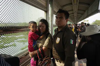 Escoltados por funcionarios mexicanos de inmigración, migrantes de un grupo de 50 que fueron elegidos por la organización Casa Migrante caminan a través del puente Puerto Nuevo desde Matamoros, México, el viernes 12 de mayo de 2023, con el fin de ser procesados por funcionarios estadounidenses de inmigración. Ello ocurrió al día siguiente de que Estados Unidos cancelara las restricciones al asilo implementadas por la pandemia de COVID-19, conocidas como Título 42. Según funcionarios mexicanos de inmigración, se organizará a los migrantes para que crucen en grupos de 50. (AP Foto/Fernando Llano)