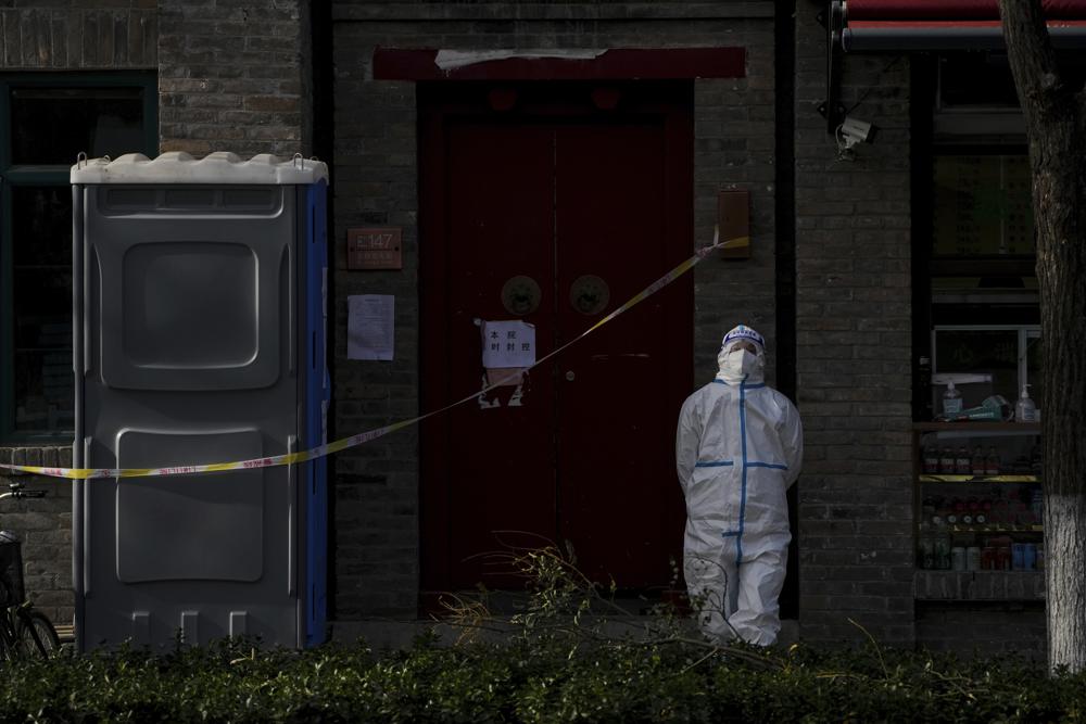 A worker in protective gear stands guard near caution tape placed in a locked down neighborhood in Beijing, Tuesday, Nov. 29, 2022. Chinese universities are sending students home as the ruling Communist Party tightens anti-virus controls and tries to prevent more protests after crowds angered by its severe "zero COVID" restrictions called for President Xi Jinping to resign in the biggest show of public dissent in decades. (AP Photo/Andy Wong)