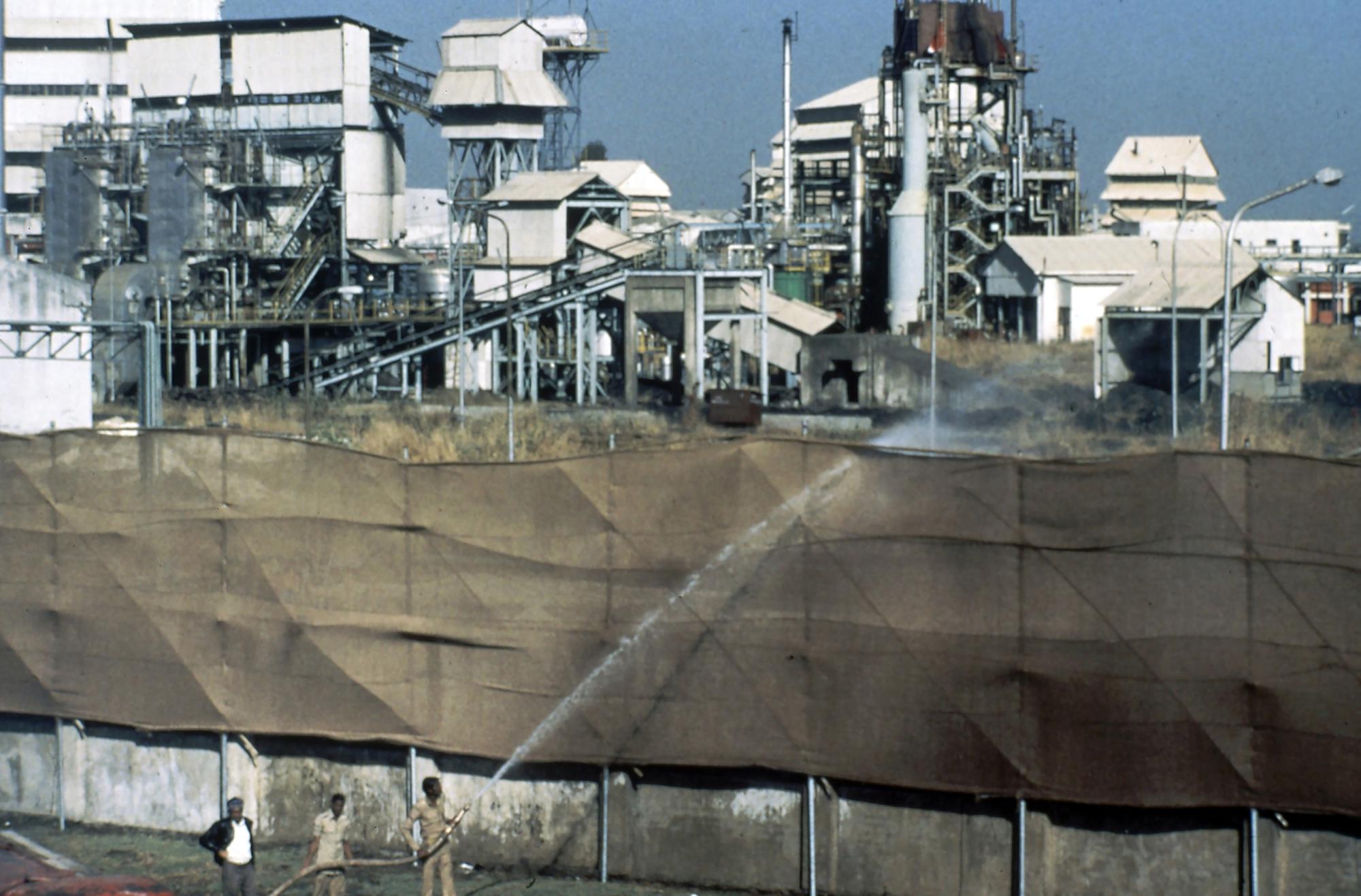 ARQUIVO - Bombeiros usam uma mangueira para molhar telas de lona nos limites da fábrica para evitar a propagação de gases perigosos na fábrica da Union Carbide em Bhopal, Índia, em dezembro de 1984. Em 3 de dezembro de 1984, a fábrica de pesticidas administrada pela Union Carbide vazou cerca de 40 toneladas de gás mortal isocianato de metila no ar, matando cerca de 15.000 pessoas e afetando pelo menos mais 500.000. A Dow Chemical Co., com sede em Michigan, assumiu a Union Carbide em 2001. (AP Photo/Peter Kemp, Arquivo)