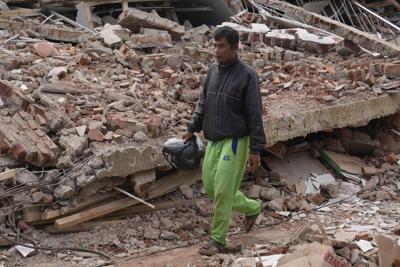 Enjot, center, who like many Indonesians only use one name, walks along the ruins of a building flattened to the ground during Monday's earthquake in Cianjur, West Java, Indonesia, Tuesday, Nov. 22, 2022. Enjot was out tending to his cows when the earth started to shake around him. Before he could even comprehend what was going on, his daughter was on the phone to tell him the earthquake had brought down his house. By Tuesday, he would learn that 11 of his relatives were among those killed in the earthquake, whose epicenter was only a few kilometers (miles) south of his village. (AP Photo/Tatan Syuflana)