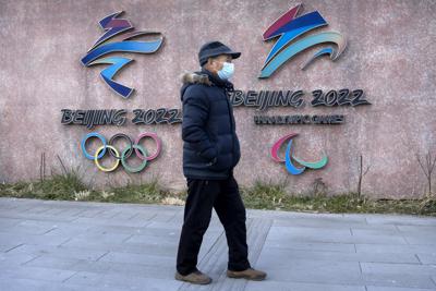 Un hombre, con mascarilla para protegerse del coronavirus, pasa por delante de los logos de los Juegos Olímpicos y Paralímpicos de Invierno de Beijing 2022, en el exterior de la sede del comité organizador, en Beijing, el 16 de diciembre de 2021. (AP Foto/Mark Schiefelbein)