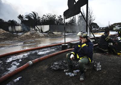 Dos bomberos descansan en el sitio de un incendio en un almacén de petróleo, el martes 9 de agosto de 2022, en Matanzas, Cuba. (Yamil Lage, foto compartida vía AP)