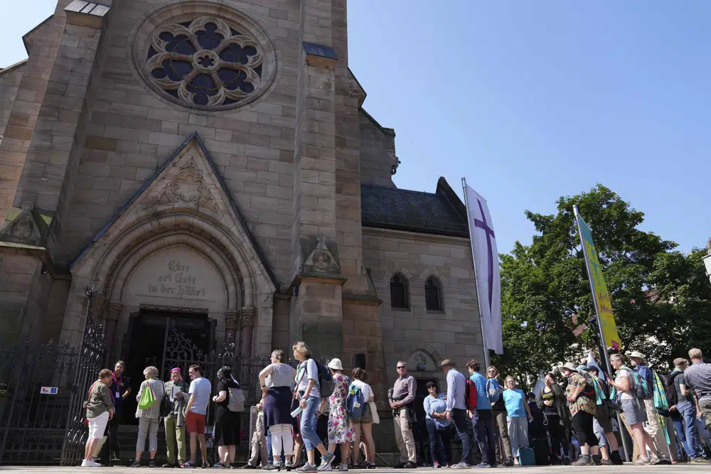 People queue for a church service in Nuremberg, Germany, Friday, June 9, 2023. Hundreds of German Protestants have attended a church service in Bavaria that was generated almost entirely by artificial intelligence. The service was created by ChatGPT and Jonas Simmerlein, a theologian and philosopher from the University of Vienna. The ChatGPT chatbot, personified by different avatars on a huge screen above the altar, led the more than 300 people through 40 minutes of prayer, music, sermons and blessings. (AP Photo/Matthias Schrader)