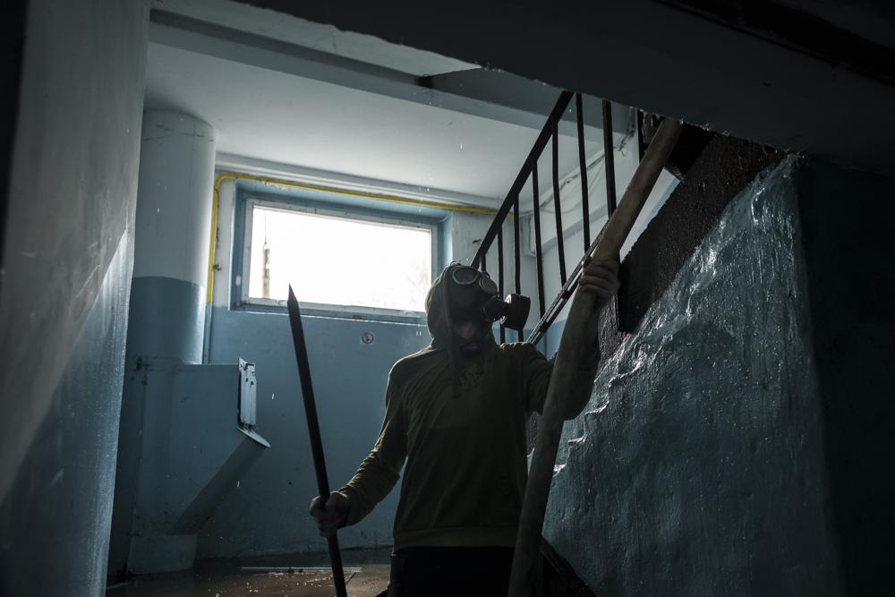 A man wearing a gas mask helps firefighters extinguish a fire on a residential building following a Russian bombardment in Kharkiv, Ukraine, Thursday, April 21, 2022. (AP Photo/Felipe Dana)