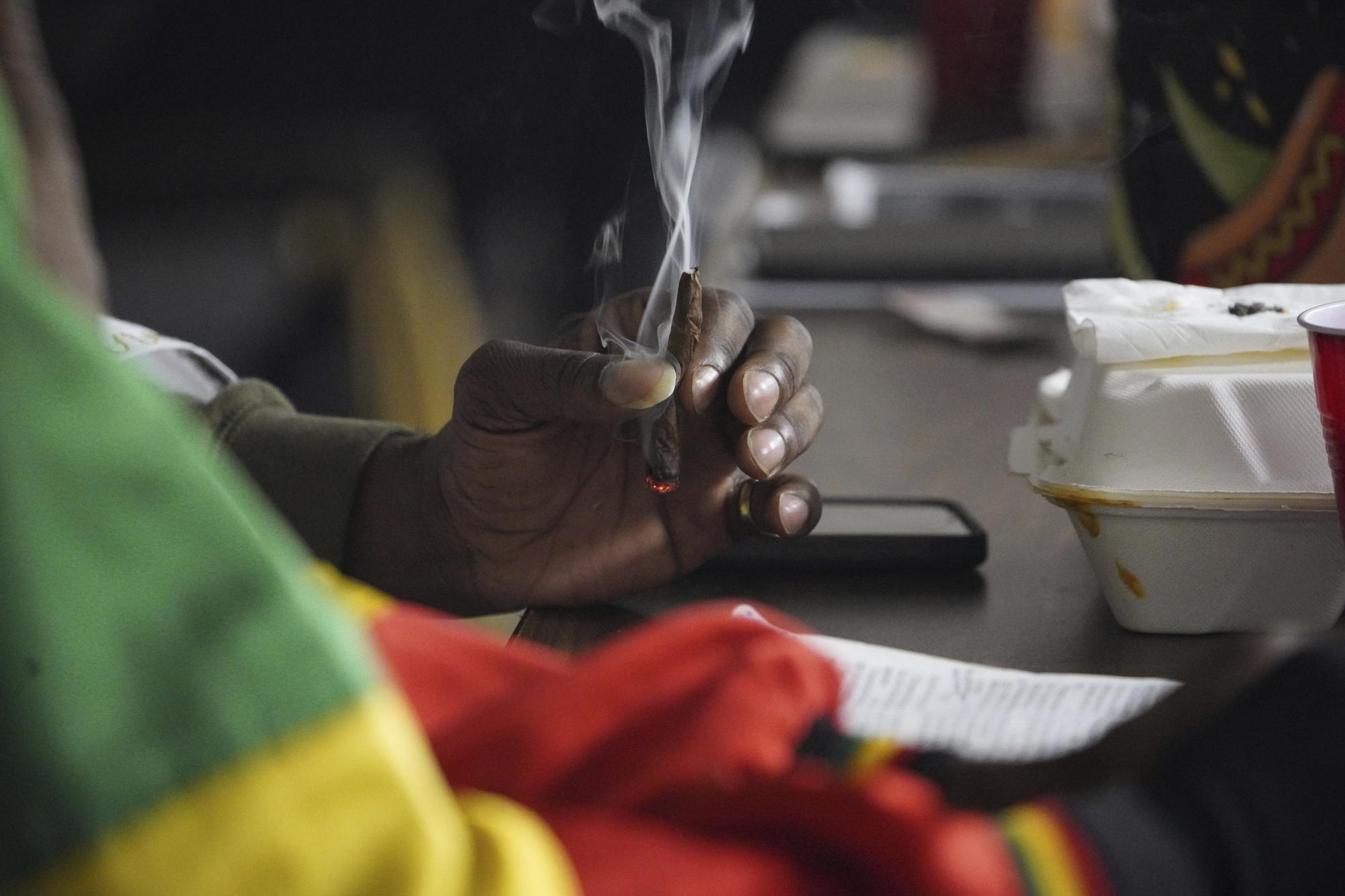 Un asistente Rastafari sostiene un cigarrillo de cannabis durante un evento de la Coalición Rastafari que marca el 91 aniversario de la coronación del difunto emperador etíope Haile Selassie I en Columbus, Ohio, el martes 2 de noviembre de 2021. A medida que la opinión pública y la política continúan cambiando en los EE. UU. y en todo el mundo hacia el uso de la marihuana, algunos seguidores de Rastafari cuestionan su lugar en el futuro de la hierba que consideran sagrada.  (Foto AP / Emily Leshner)