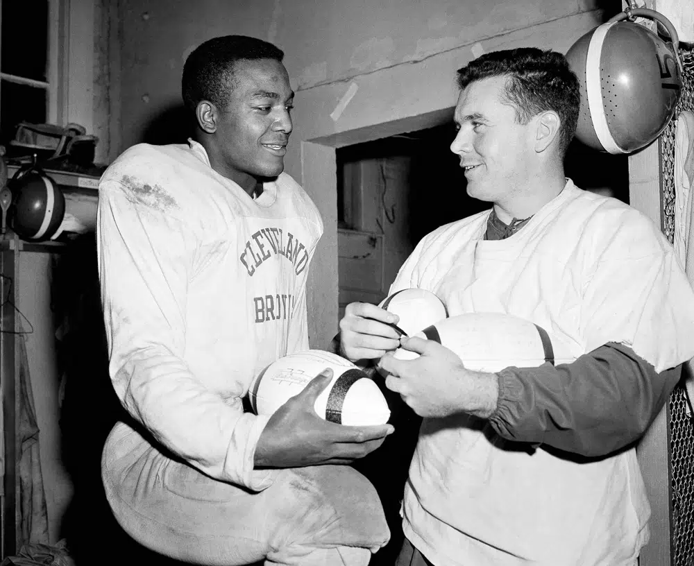 FILE - Cleveland Browns fullback Jim Brown, left, and quarterback Tommy O'Connell, shown autographing footballs, are set for National Football League championship game with the Detroit Lions at Briggs Stadium in Detroit on Sunday, Dec. 27, 1957. NFL legend, actor and social activist Jim Brown passed away peacefully in his Los Angeles home on Thursday night, May 18, 2023, with his wife, Monique, by his side, according to a spokeswoman for Brown's family. He was 87. (AP Photo/Julian Wilson, File)