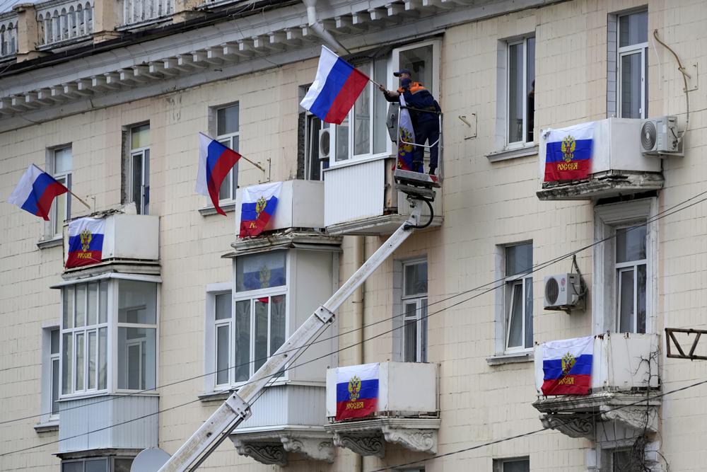 Trabajadores cuelgan banderas rusas en un edificio de apartamentos en Luhansk, Ucrania, el martes 27 de septiembre de 2022. (AP Foto)