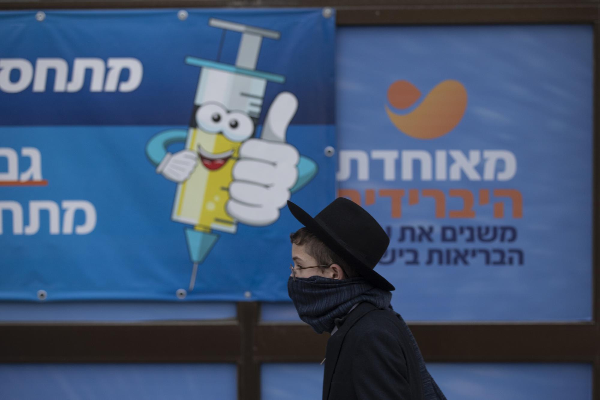 An Ultra-Orthodox Jewish youth walks past a coronavirus vaccination center, in Jerusalem, Wednesday, Dec. 22, 2021. From South African undertakers to ultra-Orthodox Israeli rabbis, an unconventional cadre of people has joined global efforts to increase COVID-19 vaccination rates. Launching campaigns that traditionally have been the realm of public health authorities, they’re opening church doors, going door to door, village to village, touting the benefits of vaccination, sometimes making shots available on the spot.  (AP Photo/Oded Balilty)