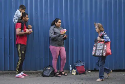Los migrantes venezolanos Junior Bucela, izquierda, y su esposa Yorlaina Hernández, centro, venden golosinas en una calle de San José, Costa Rica, 6 de diciembre de 2022. (AP Foto/Carlos Gonzalez)
