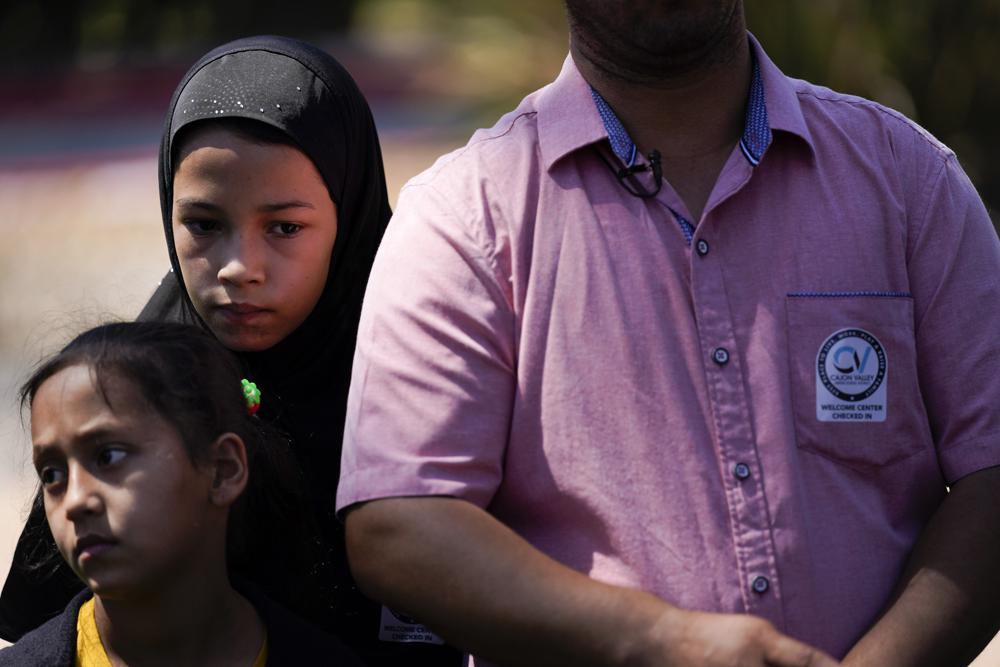 Palwasha Faizi, 10, above left, stands behind her sister, Parwana Faizi, 7, and alongside her father, Mohammad Faizi, during a news conference Thursday, Sept. 2, 2021, in El Cajon, Calif. The family were visiting relatives in Afghanistan in August, and were forced to escape as the Taliban seized power. Several families who live in the San Diego suburb of El Cajon spoke to reporters Thursday for the first time since returning from Afghanistan, where they described their harrowing escape after the Taliban seized power. (AP Photo/Gregory Bull)