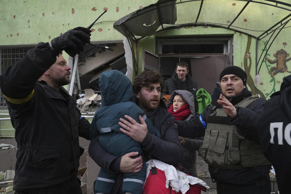 A man carries his child away from a damaged maternity hospital in Mariupol, Ukraine, Wednesday, March 9, 2022. (AP Photo/Evgeniy Maloletka)