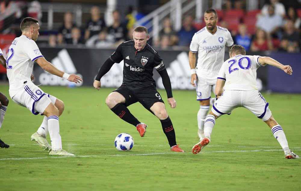 FILE - D.C. United forward Wayne Rooney (9) dribbles the ball against Orlando City midfielder Oriol Rosell (20) and defender Shane O'Neill, left, during the first half of an MLS soccer match, Sunday, Aug. 12, 2018, in Washington. Wayne Rooney arrived in America with D.C. United in 2018 at age 32. Rooney played 1½ seasons in Washington, scoring 23 goals in 48 regular season appearances, but his connection with the club went beyond what he provided on the field. (AP Photo/Nick Wass, File)