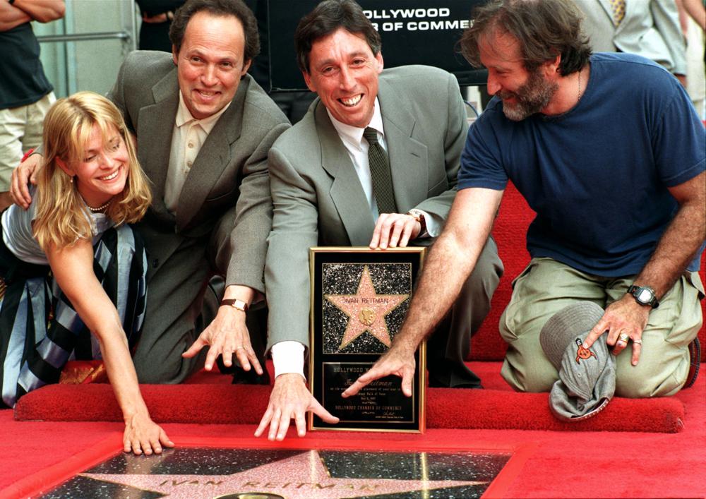 FILE - Producer and director Ivan Reitman, center, is honored with a star on the the Hollywood Walk of Fame, on the Hollywood Boulevard, on May 5, 1997, in the Hollywood section of Los Angeles. From left, actors Natasha Kinski, Billy Crystal, and Robin Williams, right, participate in the event. Reitman, the influential filmmaker and producer behind beloved comedies from “Animal House” to “Ghostbusters,” has died.  Reitman passed away peacefully in his sleep Saturday night, Feb. 12, 2022, at his home in Montecito, Calif., his family told The Associated Press.  He was 75. (AP Photo/ Damian Dovarganes, File)