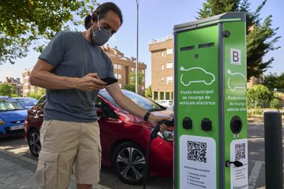 Un individuo revisa su teléfono mientras carga un auto eléctrico en Rivas Vaciamadrid, España, el 15 de junio del 2021. La escasez de sitios públicos donde cargar los autos y su precio son dos factores que conspiran contra los vehículos eléctricos en España, pero el gobierno espera dar impulso a este sector usando fondos de alivio de la UE por la pandemia. (AP Photo/Manu Fernández)