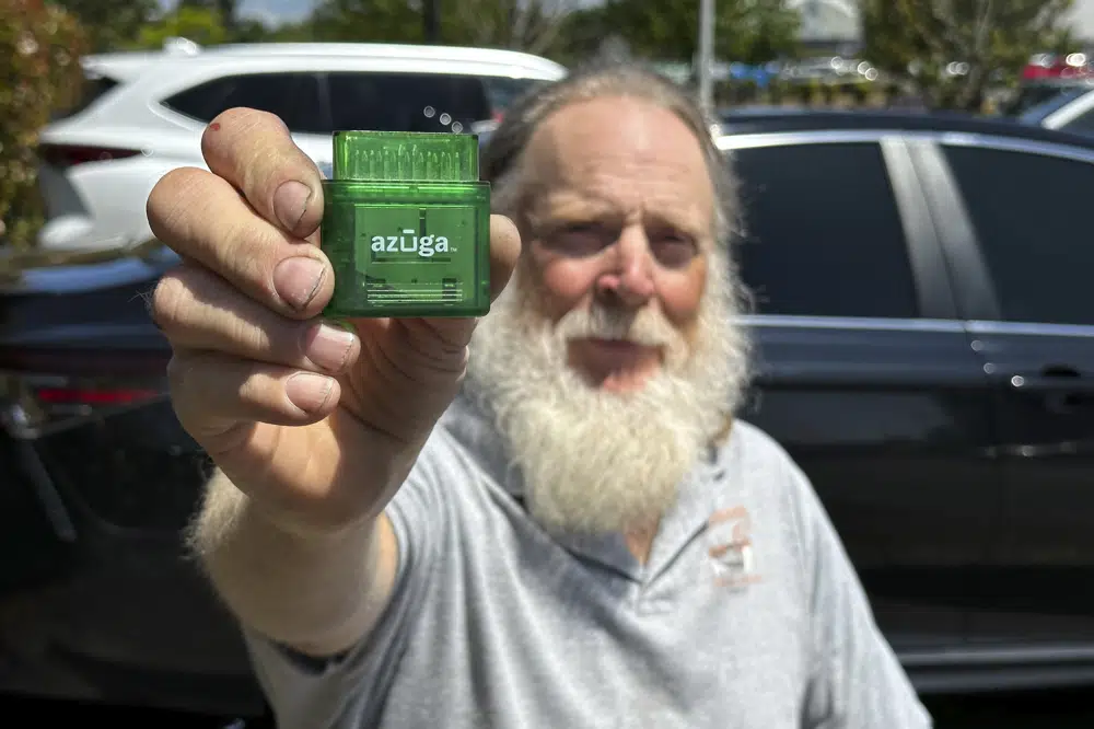 Evan Burroughs, who touts the virtues of an Oregon pilot program that charges motorists by the distance their vehicle travels rather than the gas it uses, displays a tracking device the program uses, in Salem, Ore., on Wednesday June 21, 2023. U.S. states are experimenting with road usage charging programs aimed at one day replacing motor fuel taxes, which are generating less each year, in part due to fuel efficiency and the rise of electric cars. (AP Photo/Andrew Selsky)