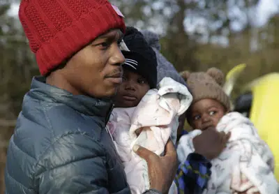 El migrante haitiano Gerson Solay, con su hija Bianca en brazos, y su familia entran a Canadá por el cruce no oficial de Roxham Road al norte de Champlain, Nueva York, viernes 24 de marzo de 2023. (AP Foto/Hasan Jamali)