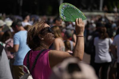 FILE - A tourist uses a fan to shade her face from the sun whilst waiting to watch the Changing of the Guard ceremony outside Buckingham Palace, during hot weather in London, July 18, 2022. Scientists said the heat wave in England and Wales on July 18 and 19 was definitely turbocharged by human-caused climate change, according to a study released Thursday, July 28, by the World Weather Attribution. (AP Photo/Matt Dunham, File)