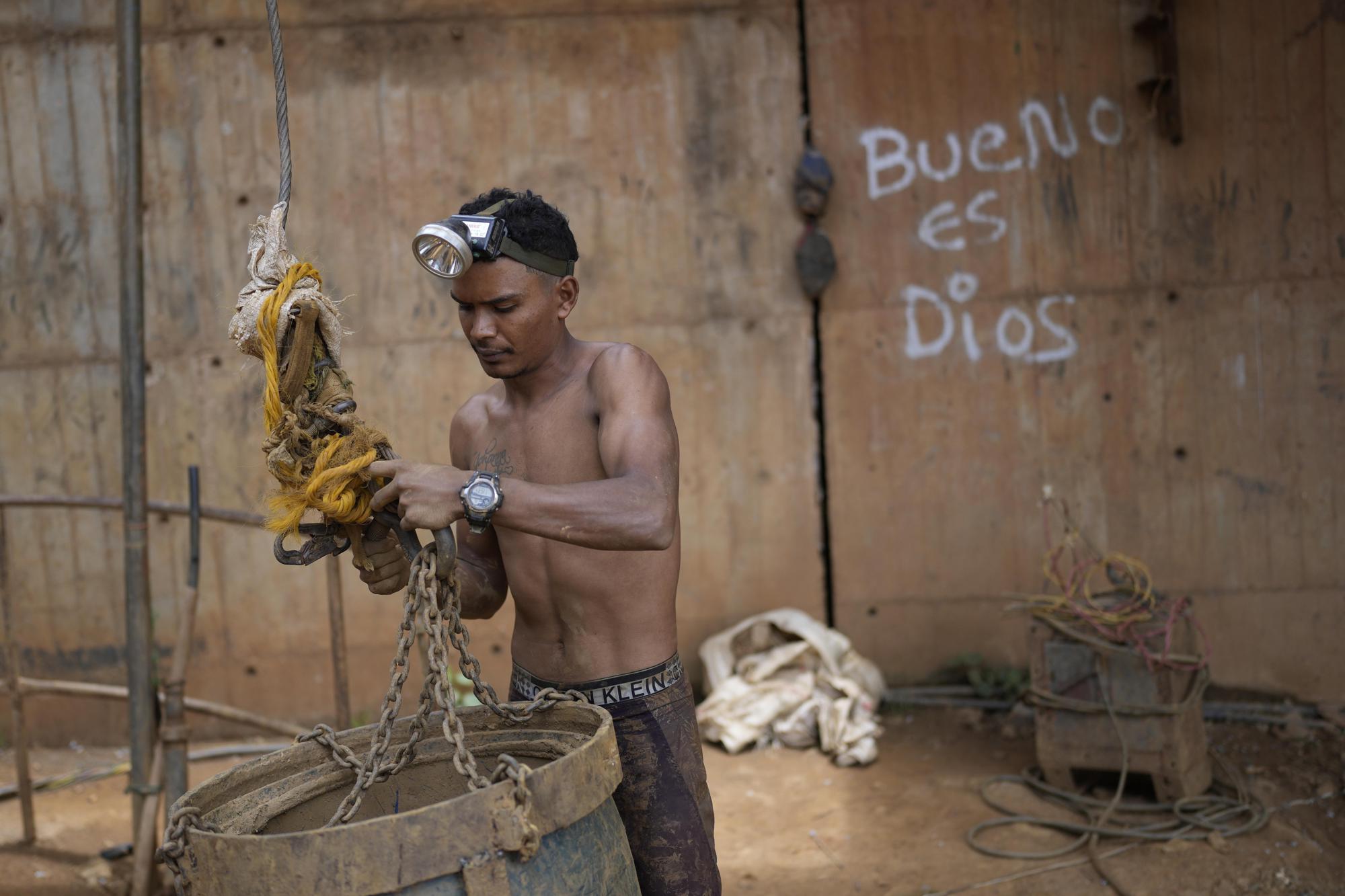 Un trabajador conecta un balde grande a un sistema de poleas para transportar rocas y herramientas por un pozo en una mina de oro subterránea en El Callao, estado de Bolívar, Venezuela, el viernes 28 de abril de 2023. (Foto AP/Matias Delacroix)