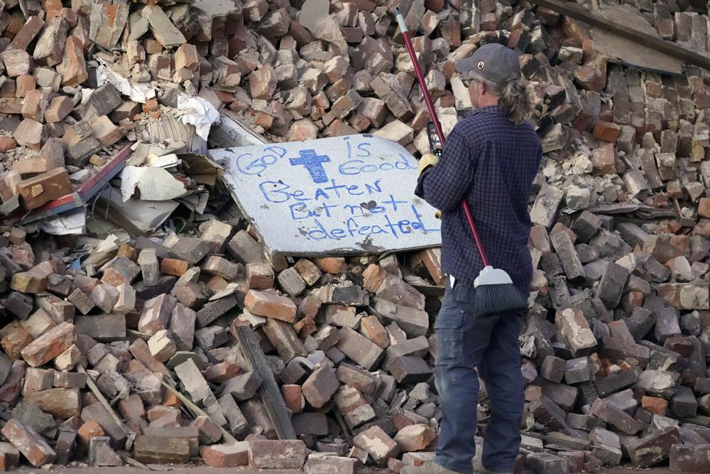 Rick Vincent, of Newaygo, Mich., reads a sign placed on a pile of building rubble as he stops work at the end of the day, Sunday, Dec. 12, 2021, in Mayfield, Ky. Vincent, a retired teacher, has come to Mayfield on his own to volunteer to help in the cleanup effort after tornadoes and severe weather caused catastrophic damage across several states Friday, killing multiple people. (AP Photo/Mark Humphrey)