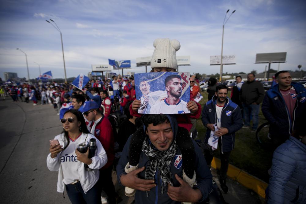 Una niña sostiene una foto de Luis Suárez al ser alzada por su padre afuera del aeropuerto durante el recibimiento al frente, el domingo 31 de julio de 2022. Suárez jugará con Nacional de Montevideo. (AP Foto/Matilde Campodónico)