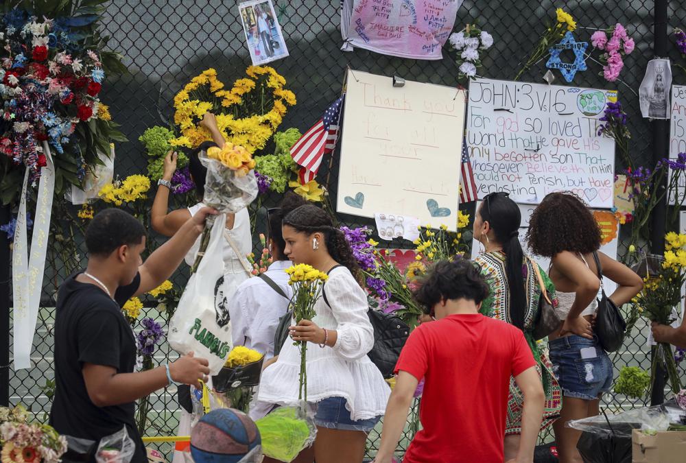 Los voluntarios junto con los lugareños reemplazan las flores muertas por otras frescas en un memorial improvisado para las víctimas del derrumbe del edificio de condominios Champlain Towers South, el martes 6 de julio de 2021, en Surfside, Florida (Carl Juste / Miami Herald vía AP)