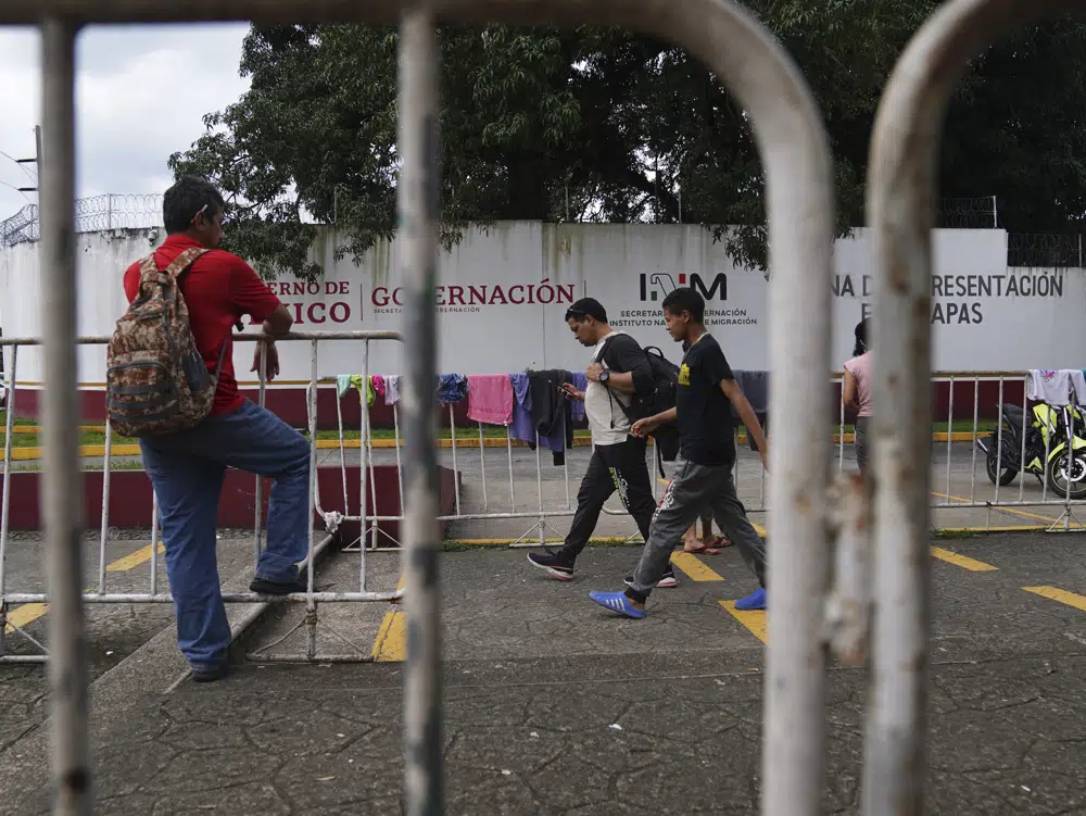 Migrantes caminan frente al Instituto Nacional de Migración en Tapachula, estado de Chiapas, México, el martes 3 de octubre de 2022. En cuando llegan al principal punto de entrada en el sur de México, pronto se dan cuenta de que la única forma de evitar la burocracia y acelerar un proceso que puede llevar meses, es pagando. (AP Foto/Marco Ugarte)