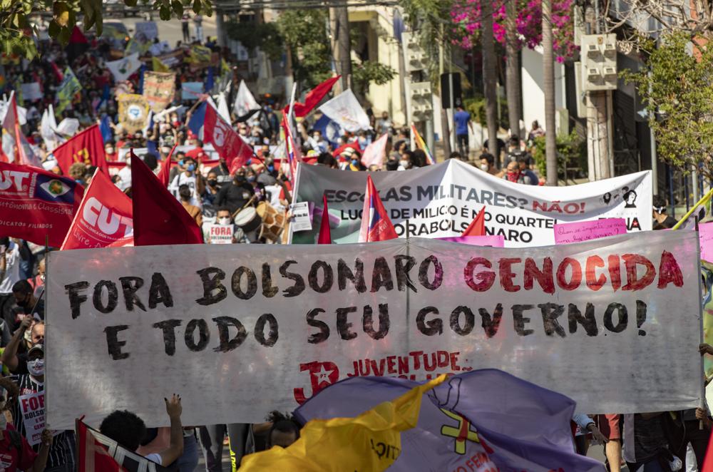 Demonstranten marschieren mit einem Banner mit portugiesischer Botschaft; "Verschwinden Sie den Völkermord Bolsonaro und Ihre gesamte Regierung" während eines Protests gegen den brasilianischen Präsidenten Jair Bolsonaro und seinen Umgang mit der Pandemie und der Wirtschaftspolitik Demonstranten sagen, dass dies den Interessen der Armen und der Arbeiterklasse schadet, in Cuiaba, Brasilien, Samstag, 19. Juni 2021 June (AP Foto/Andre Penner)