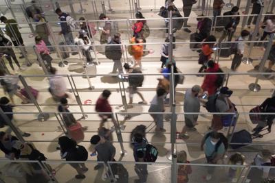 Viajeros con mascarillas como medida de prevención contra el contagio de coronavirus hacen fila para una revisión de seguridad en el aeropuerto Love Field, en Dallas, el viernes 31 de diciembre de 2021. (AP Foto/LM Otero)