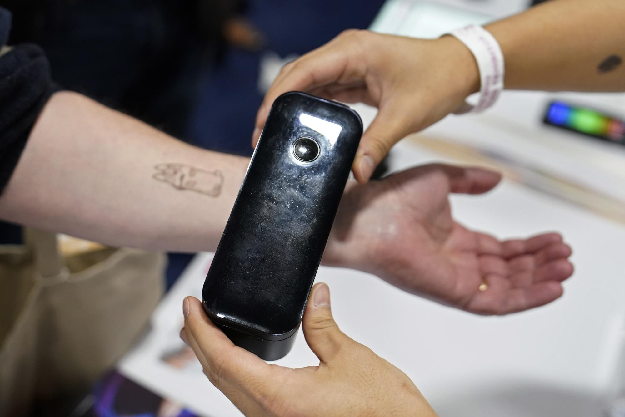 An exhibiter apples a temporary tattoo with a Prinker digital temporary tattoo device during CES Unveiled before the start of the CES tech show, Tuesday, Jan. 3, 2023, in Las Vegas. The device allows the user to print a temporary tattoo in cosmetic ink. (AP Photo/John Locher)