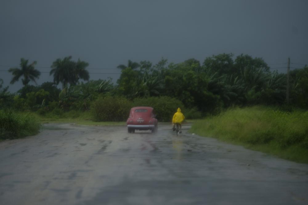 Un hombre se desplaza en una bicicleta junto a un automóvil bajo la lluvia causada por el huracán Ida, en Guanimar, provincia de Artemisa, Cuba, el sábado 28 de agosto de 2021. (Foto AP/Ramón Espinosa)