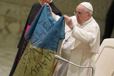 El papa Francisco alza una bandera ucraniana que le llevaron desde Bucha, Ucrania, durante su audiencia general semanal en la sala Pablo VI, Ciudad del Vaticano, miércoles 6 de abril de 2022. (AP Foto/Alessandra Tarantino)