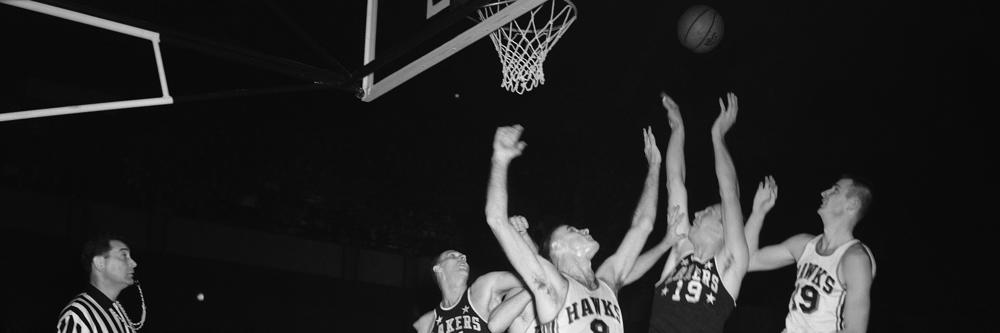 Vern Mikkelsen of Minneapolis Lakers is closely guarded by Bob Pettit and Hub Reed (19), both of St. Louis Hawks, as he leaps for a rebound in first period of National Basketball Association game November 22, 1958. At left is Larry Faust (14) of Lakers. (AP Photo)
