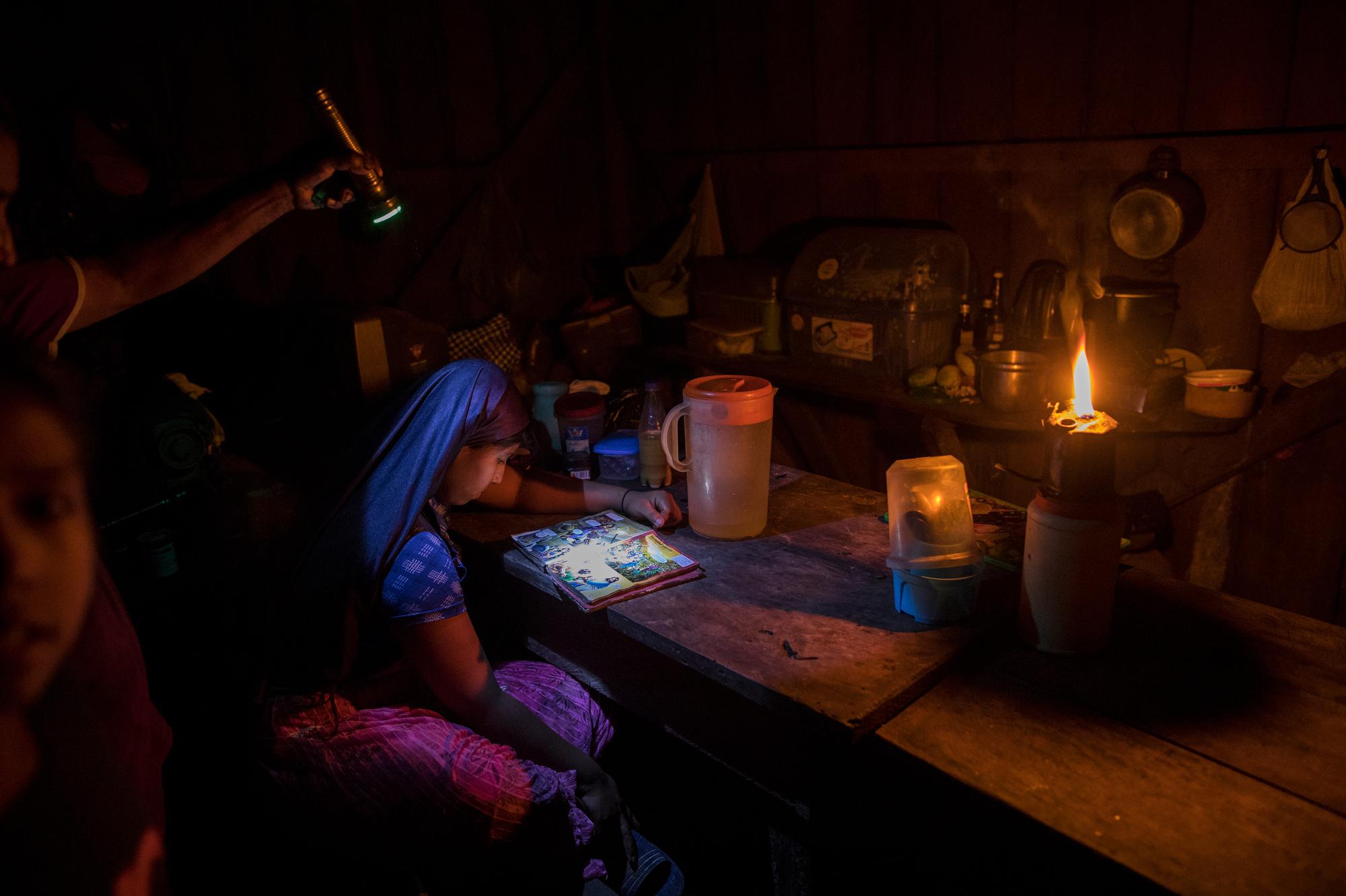 With the aid of a flashlight and a kerosene flame, 12-year-old Zairi Olivia, a member of the evangelical Christian sect Israelites of the New Universal Pact, looks at The Children's Illustrated Bible in her house in Jose Carlos Mariategui, Peru, a village in the Amazon rainforest, on March 31, 2021. (AP Photo/Rodrigo Abd)
