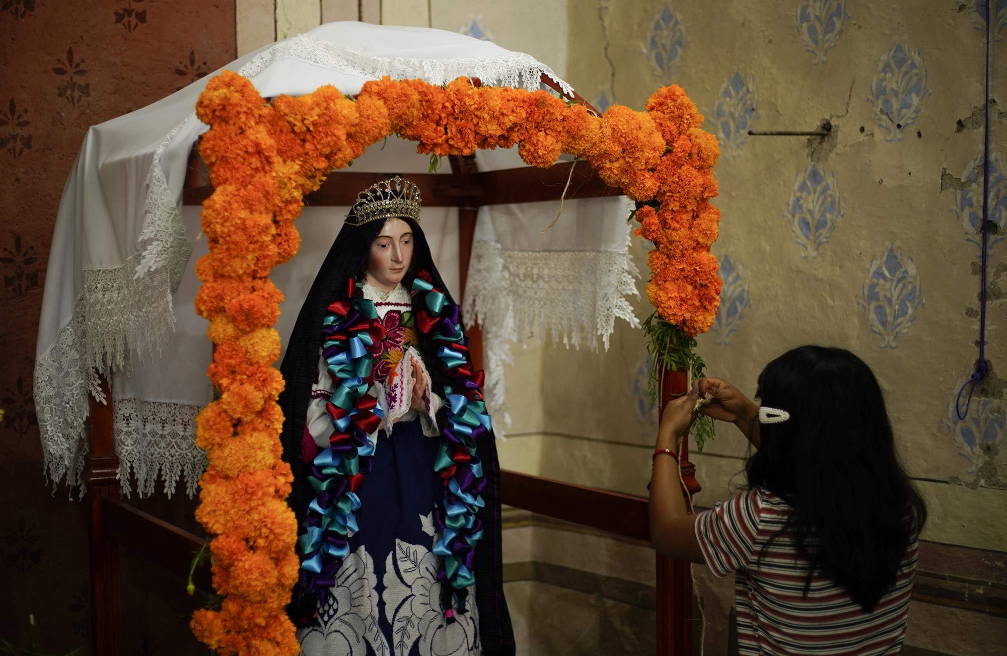 A woman adorns a religious image with Mexican marigold flowers known as Cempasuchil, inside the church at the Arocutin municipal cemetery as people begin to arrive to pay their respects to their dead in Arocutin, Michoacan, Sunday, Oct. 31, 2021. (AP Photo/Eduardo Verdugo)