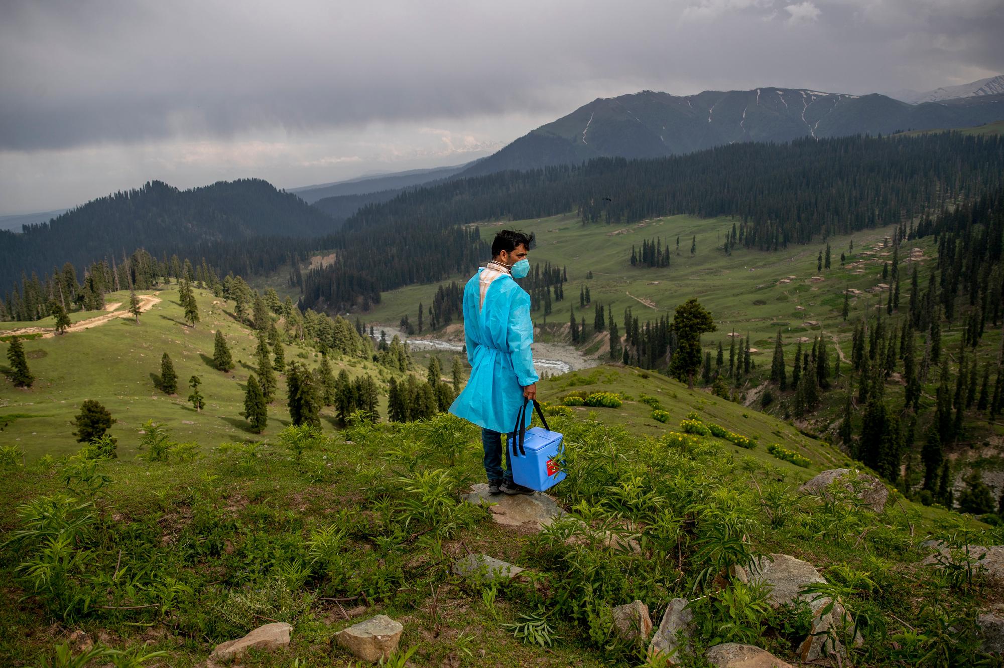 Health care worker Nazir Ahmed carries a cooler with vaccines and looks out from a hillock for Kashmiri shepherds to vaccinate in Tosamaidan, southwest of Srinagar, Indian controlled Kashmir, on June 21, 2021. (AP Photo/Dar Yasin)