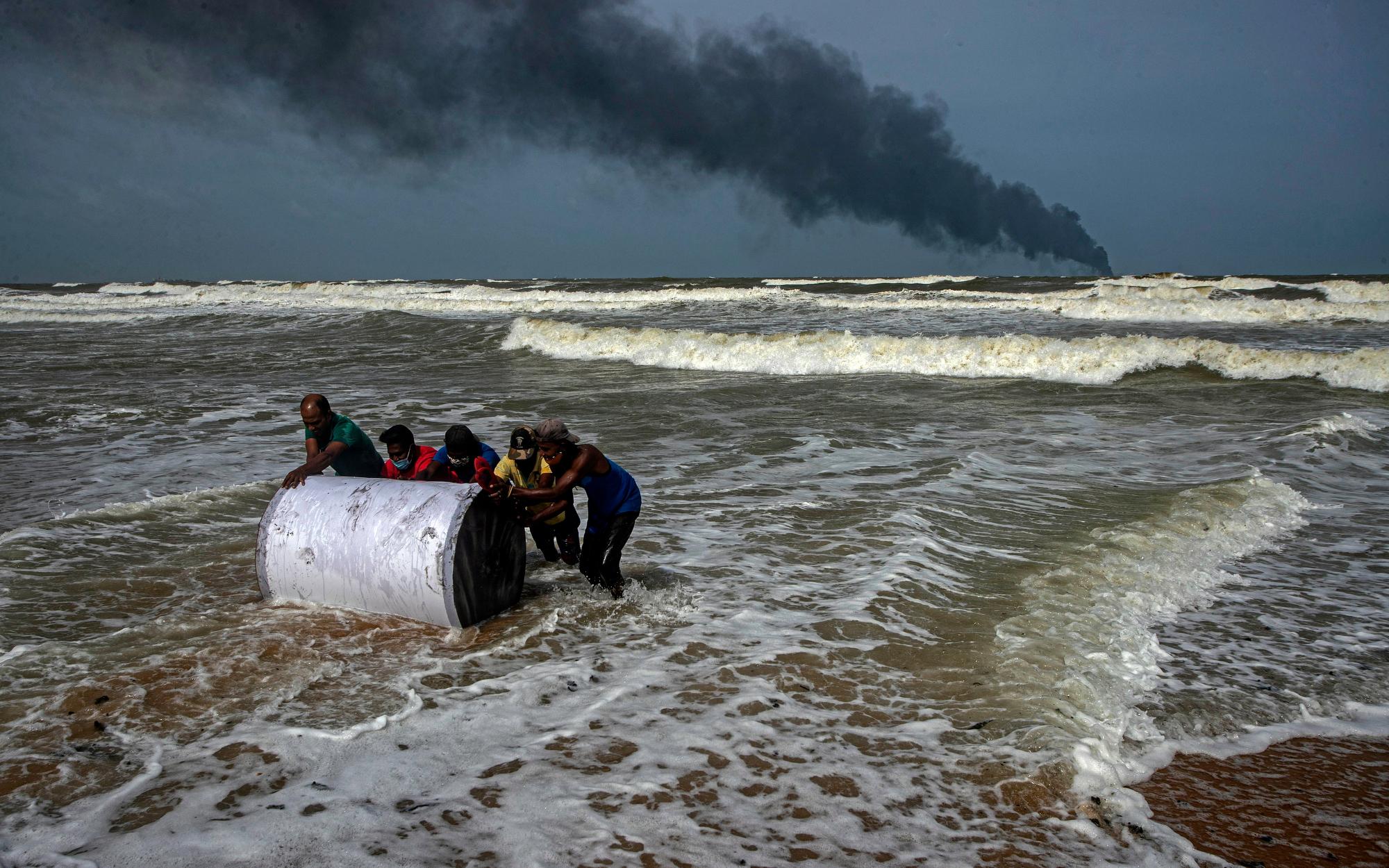 Impoverished Sri Lankans salvage debris that washed ashore on May 26, 2021, from the burning Singaporean ship X-Press Pearl, which caught fire several days earlier off the coast of Colombo, Sri Lanka. (AP Photo/Eranga Jayawardena)