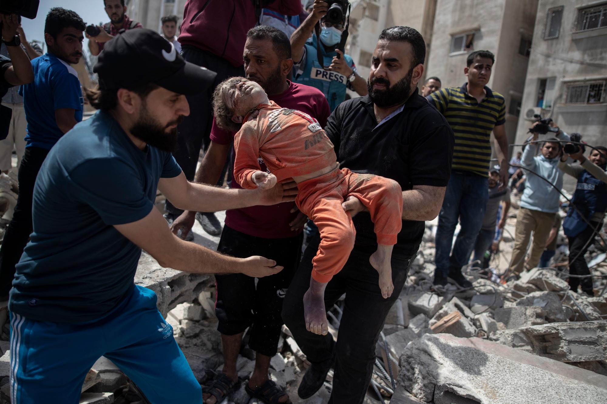 Men carry a dead child pulled from the rubble of a destroyed residential building in Gaza City following Israeli airstrikes on May 16, 2021, that flattened three buildings and killed at least two dozen people, according to medics. (AP Photo/Khalil Hamra)