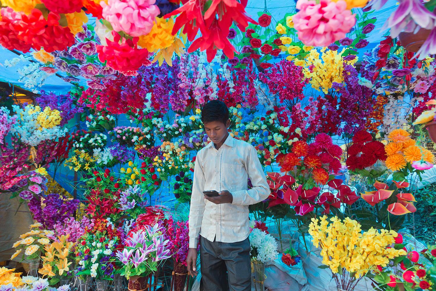 FILE - In this Sept. 16, 2018, file photo,  an Indian youth checks his phone as he sells plastic flowers at a local fair in Dharmsala, India. (AP Photo/Ashwini Bhatia, File)
