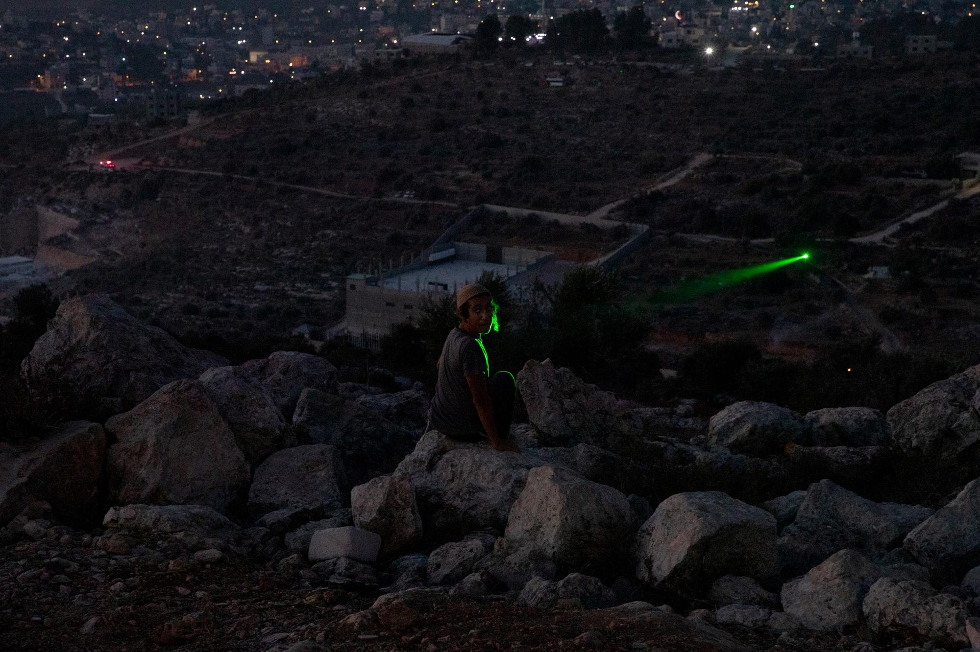 An Israeli settler is illuminated by a Palestinian protester’s laser at the recently established wildcat outpost of Eviatar near the West Bank city of Nablus, on July 1, 2021. (AP Photo/Maya Alleruzzo)