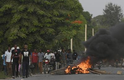 Varios hombres caminan junto a una barricada en llamas después de que cientos de trabajadores huyeran de una zona en la que se llevaron a cabo manifestaciones que se tornaron violentas cerca de la ciudad natal del difunto presidente Jovenel Moïse, el miércoles 21 de julio de 2021, en Quartier Morin, un distrito de Cap Haitien, en el norte de Haití. (AP Foto/Matías Delacroix)