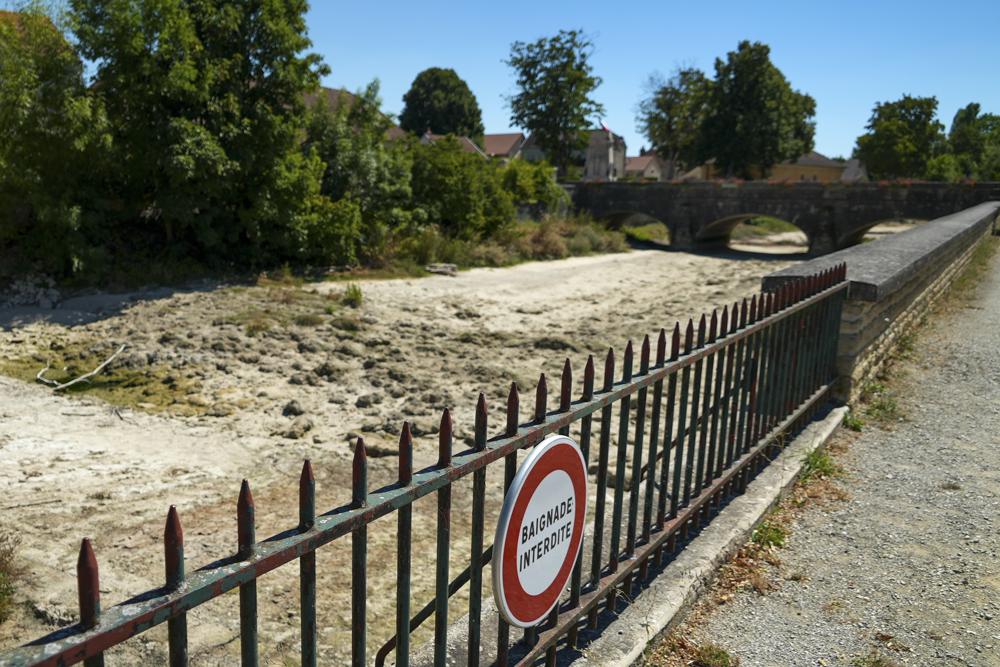 A sign on a fence near the dried-up river Tille says 'Swimming is Forbidden' in Lux, France, Tuesday Aug. 9, 2022. Burgundy, home to the source of the Seine River which runs through Paris, normally is a very green region. This year, grass turned yellow, depriving livestock from fresh food, and tractors send giant clouds of dust in the air as farmers work in their dry fields. (AP Photo/Nicholas Garriga)