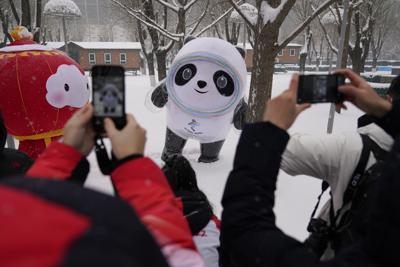 ARCHIVO - La gente toma fotos de la mascota olímpica Bing Dwen Dwen, en el centro, y la mascota paralímica Shuey Rhon Rhon, a la izquierda, en la nieve en los Juegos Olímpicos de Invierno de 2022, el 13 de febrero de 2022, en Beijing. (AP Photo/Ashley Landis, Archivo)
