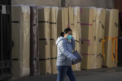 Una mujer con mascarilla pasa junto a ataúdes vacíos almacenados en el exterior de una morgue de un hospital de Beijing, el 6 de enero de 2023. (AP Foto/Andy Wong)