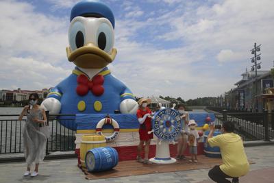 Visitantes posan para fotos ante el parque temático Disney Resort, el jueves 30 de junio de 2022 en Shanghái.  (AP Foto/Chen Si)