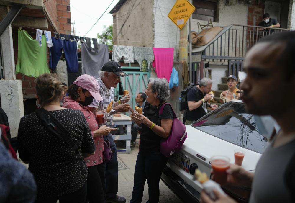 Turistas comen empanadas, una especie de pastelería rellena, durante un recorrido organizado por el barrio San Agustín de Caracas, Venezuela, el sábado 21 de agosto de 2021. El "Cumbe Tour" trae a turistas, tanto nacionales como extranjeros, al barrio de San Agustín para mostrarles cómo viven los venezolanos de menores ingresos en lo que solía ser una de las zonas más peligrosas de la ciudad. (Foto AP/Ariana Cubillos)